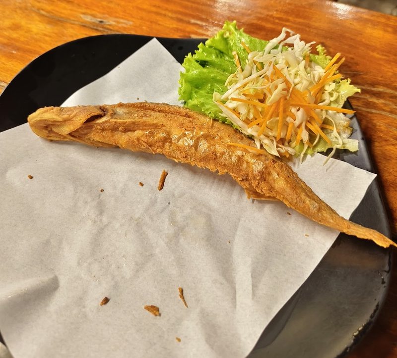 ปลาเนื้ออ่อนทอดทั้งตัวโรยกระเทียมเจียว วางบนกระดาษ มีมะละกอสับและผักสลัดข้างจาน