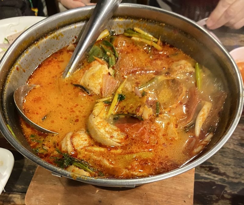 ต้มยำปลาคังน้ำสีส้มในหม้อไฟ มีชิ้นปลา พริก และสมุนไพร