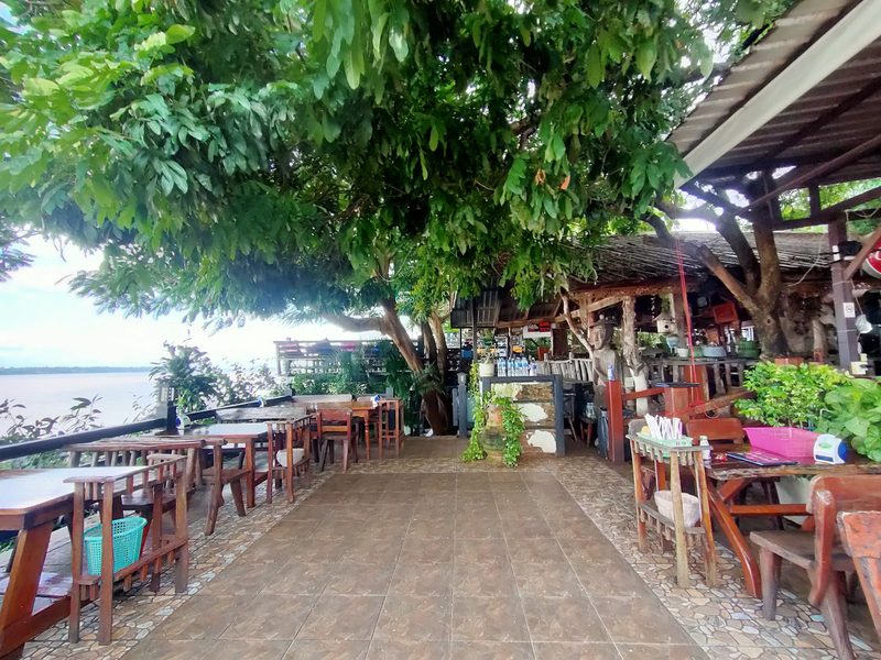 ลานปูอิฐ โต๊ะเรียงใต้ร่มไม้ข้างแม่น้ำ