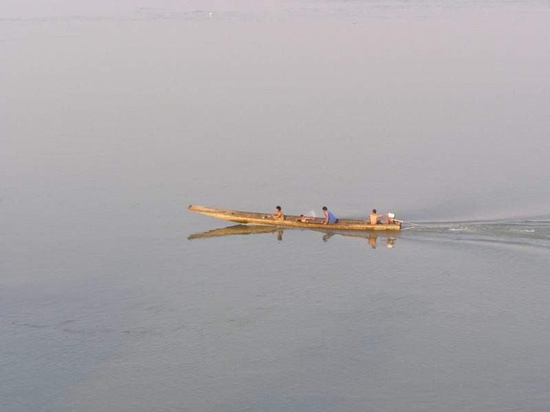 เรือหางยาวลำเล็กแล่นบนผิวน้ำเรียบในเช้าที่มีหมอก